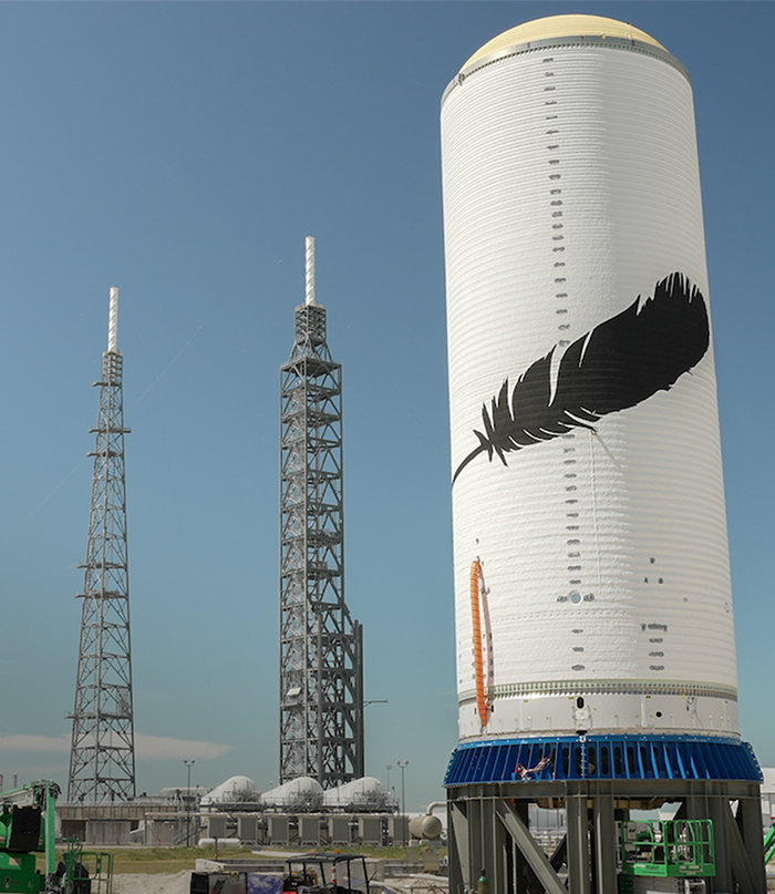 The white cylinder of New Glenn’s second stage tank stands upright with Blue Origin’s black feather painted on the side. The two lightning towers at Launch Complex 36 are visible in the background.