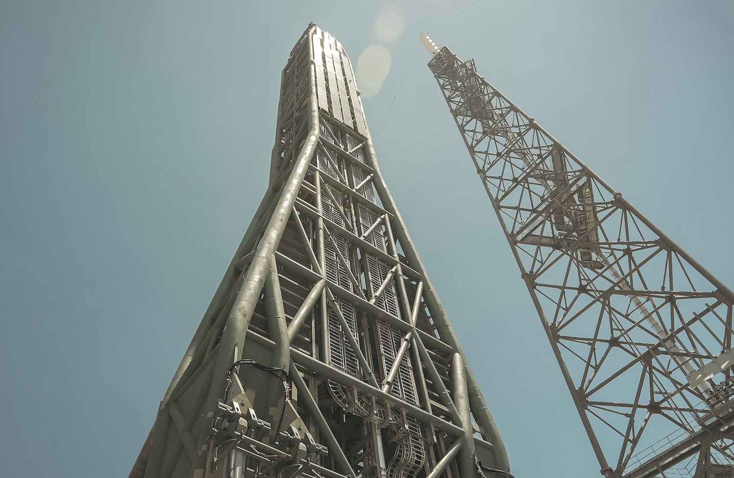 Two gray scaffolding-like towers stand against a clear blue sky. The Transport Erector (left) will support New Glenn at launch.