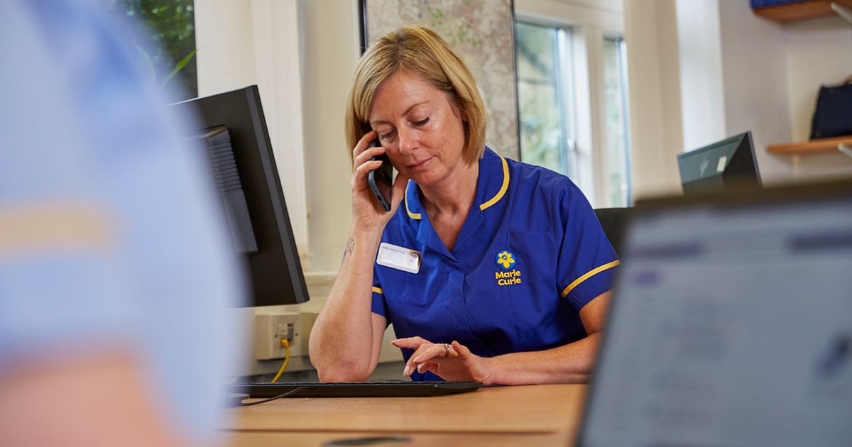 A Marie Curie Support Line Officer speaking on the phone while typing on a computer keyboard