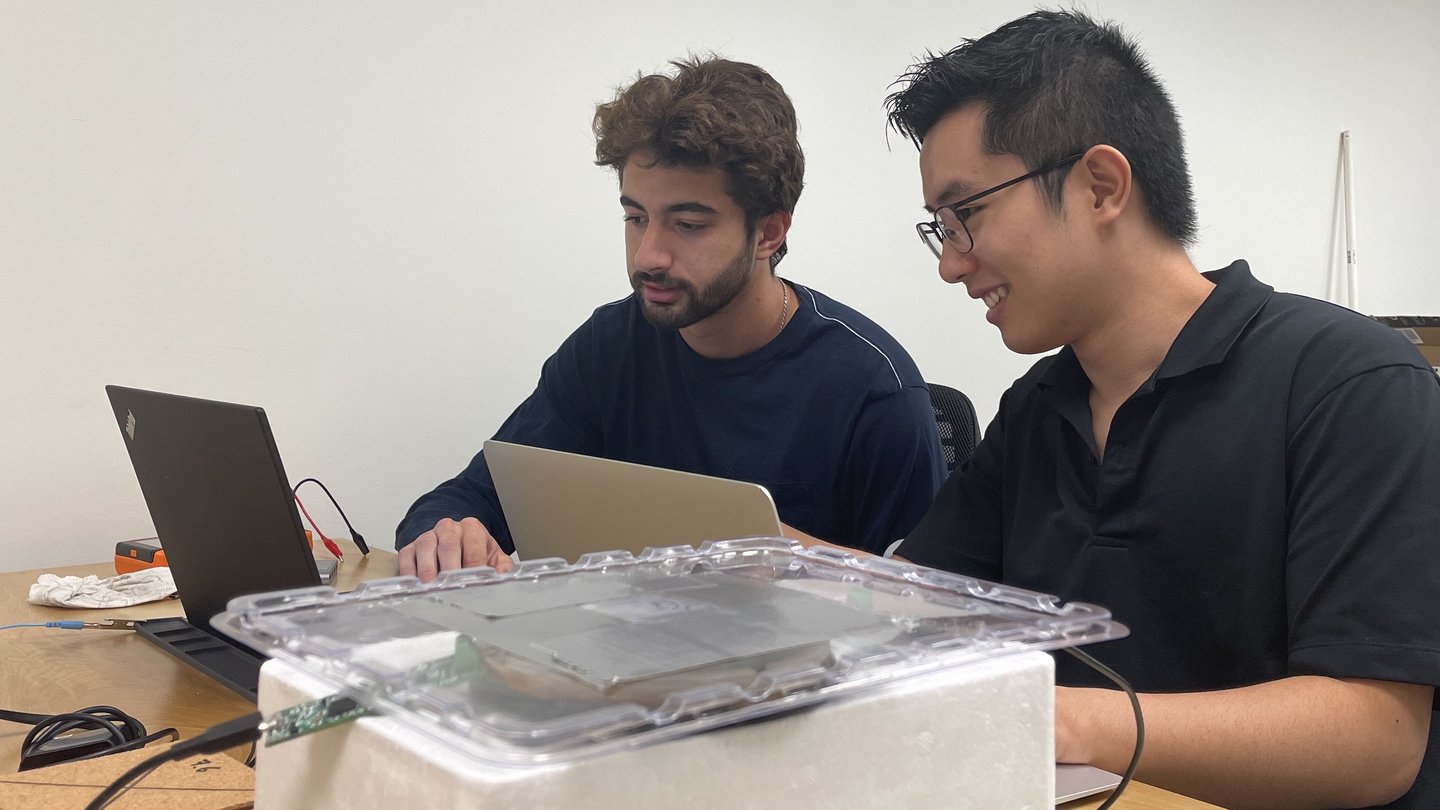 Two young men sitting in front of a laptop, smiling.