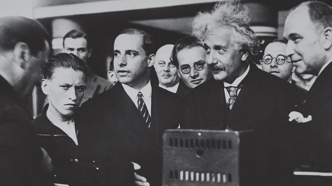 photograph from 1930 of eleven men, one of whom is Albert Einstein, gathered around a radio