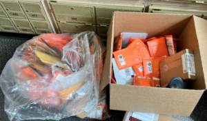 clear plastic bag filled with hundreds of envelopes next to a large cardboard box also filled with hundreds of envelopes