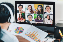 Rear view of an Asian man holding charts and talking to others in an online meeting via video conference.