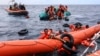 FILE - Migrants aboard a rubber boat end up in the water while others cling on to a centifloat before being rescued by a team of the Sea Watch-3, around 35 miles away from Libya, Oct. 18, 2021. 