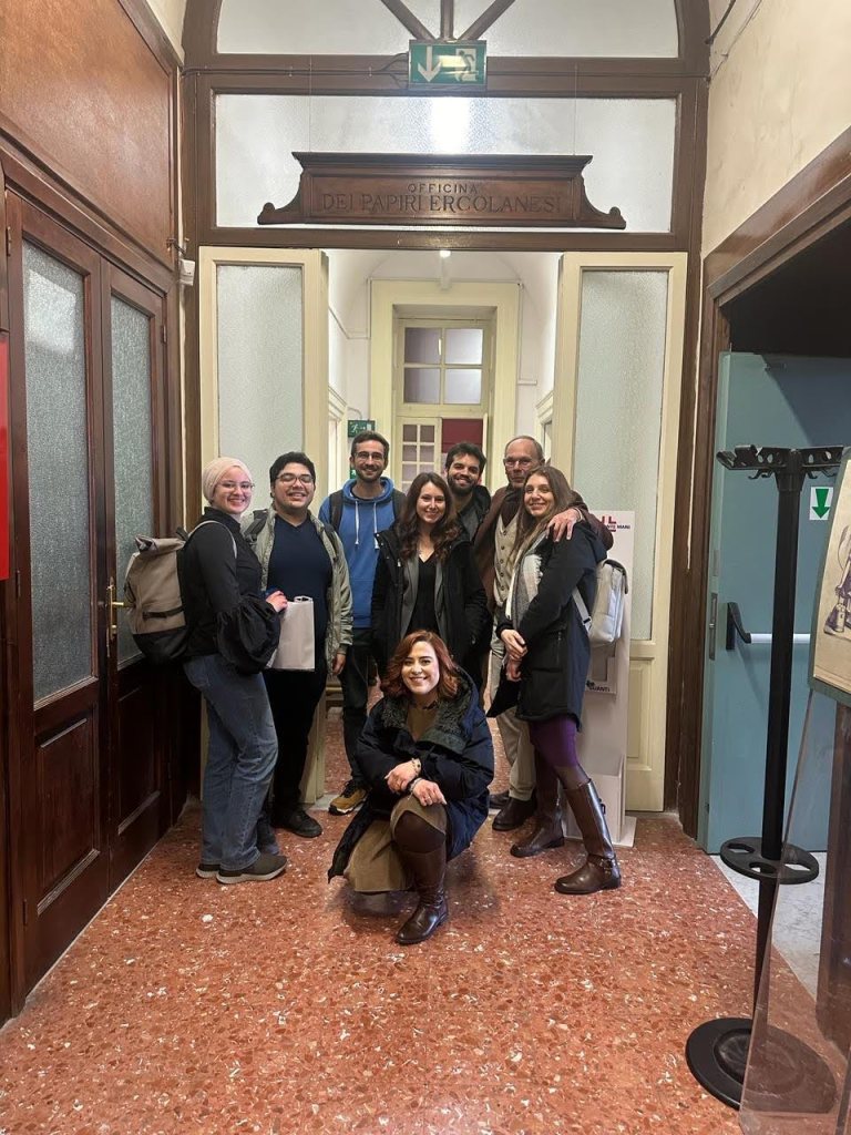 The winning team and others stand in front of a doorway in Naples, Italy, where the traveled to see the scrolls in person.