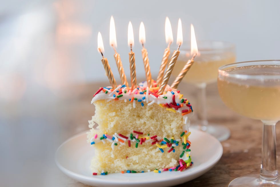 candles burning on slice of cake with sprinkles near champagne