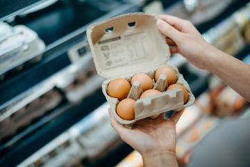 close up of young asian woman grocery shopping in a supermarket she is holding a box of fresh organic free range eggs in front of a refrigerated section healthy eating lifestyle