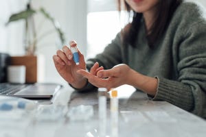 cropped shot of young woman doing finger prink blood test at home