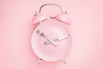 alarm clock and plate with cutlery concept of intermittent fasting, lunchtime, diet and weight loss