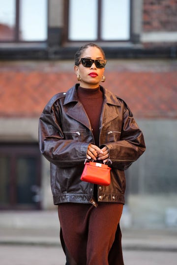 copenhagen, denmark february 02 ellie delphine wears black sunglasses, gold earrings, a dark brown high neck long dress, a dark brown shiny varnished leather oversized biker jacket, a red shiny leather micro handbag, outside helmstedt, during the copenhagen fashion week autumnwinter 2023 on february 02, 2023 in copenhagen, denmark photo by edward berthelotgetty images