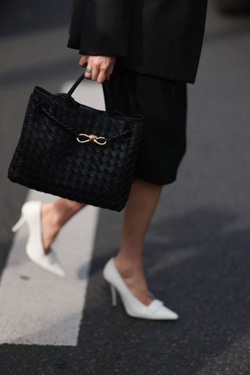 a woman carrying a black leather tote bag by bottega veneta with a black skirt and white pump while crossing the street in paris in a roundup of best laptop bags for women 2024