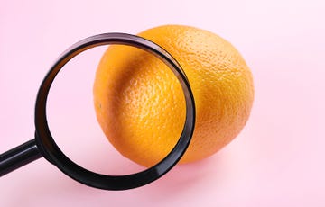 magnifying glass hovering over an orange in front of a pink background