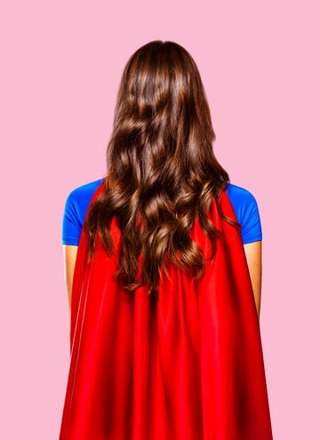 woman with brown hair wearing a red cape and blue shirt in front of pink background