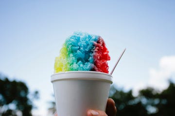 hand holding colorful snow cone against sky