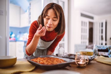 young pretty asian woman tasting a dish of pasta she prepared while serving food on the table at home