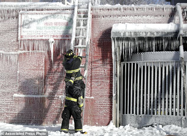 FILE- In this  Jan. 5, 2018 file photo, a Newark firefighter his held up by a colleague as he chips ice off a ladder after helping battle a five building fire in Newark, N.J. Firefighters battling blazes in the extreme cold are faced with treacherous conditions, frozen hydrants and slick surfaces that make an already difficult job even harder. Departments in colder climates prepare months ahead for the coming freeze, readying equipment and changing how they approach fires in the coldest months. (AP Photo/Julio Cortez, File)