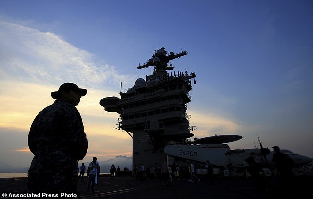 An American navy officer is silhouetted aboard the aircraft carrier USS Carl Vinson as it docks in Danang bay, Vietnam on Monday, March 5, 2018. For the first time since the Vietnam War, a U.S. Navy aircraft carrier is paying a visit to a Vietnamese port, seeking to bolster both countries' efforts to stem expansionism by China in the South China Sea. (AP Photo/ Hau Dinh)