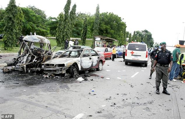 Policeman stand near a damaged car following a blast in Abuja during ceremonies for the 50th anniversary of the country's independence