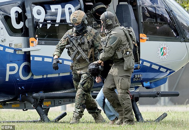 The suspect (pictured, centre) was seen getting dragged to his arraignment at the Federal Supreme Court (BGH) in Karlsruhe, Germany, today by federal police officers