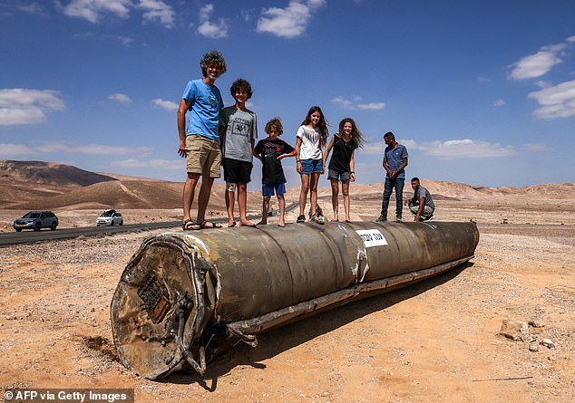 Children and adults stand on top of the remains of an Iranian missile in the Negev desert near Arad, Israel