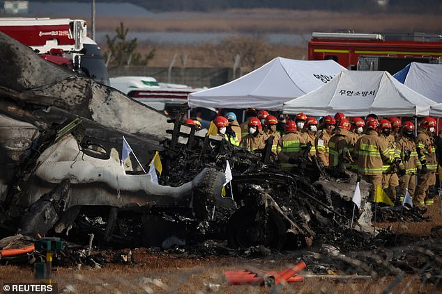 Rescue workers stand beside the wreckage as they search through the debris