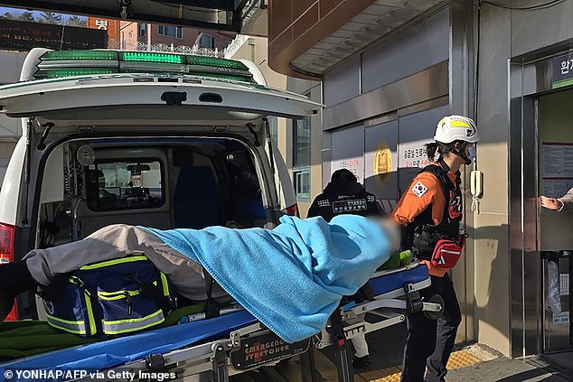 A person rescued from the wreckage is wheeled on a stretcher from an ambulance to a medical facility