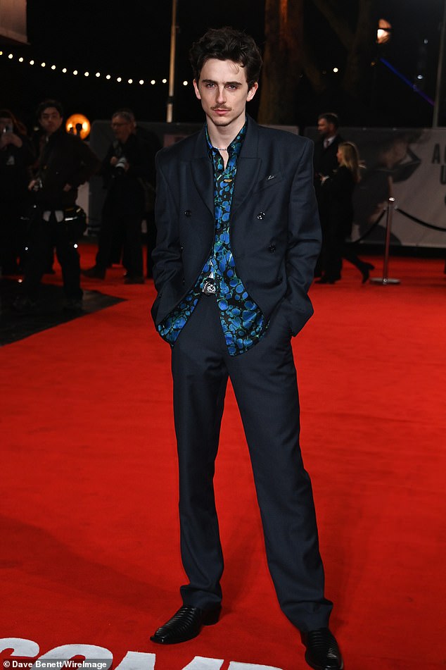 He cut a dapper figure in a black blazer and matching trousers, with a blue patterned satin shirt underneath