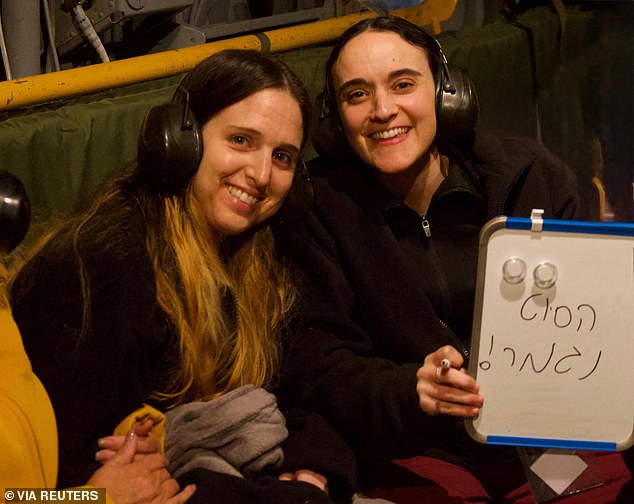 Emily Damari holds up a sign which reads in Hebrew "the nightmare is over!" as she and released Israeli hostage Doron Steinbrecher are transported to a hospital