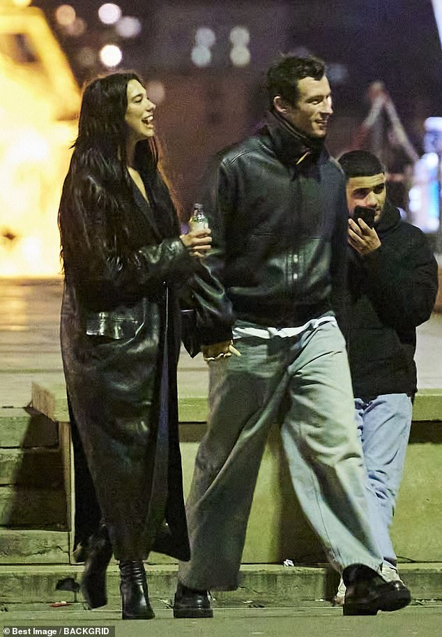 The New Rules singer wears a chic, all-black look with boots and a long trench coat for the evening walk with her fiance, who opts for a more casual leather jacket and jeans