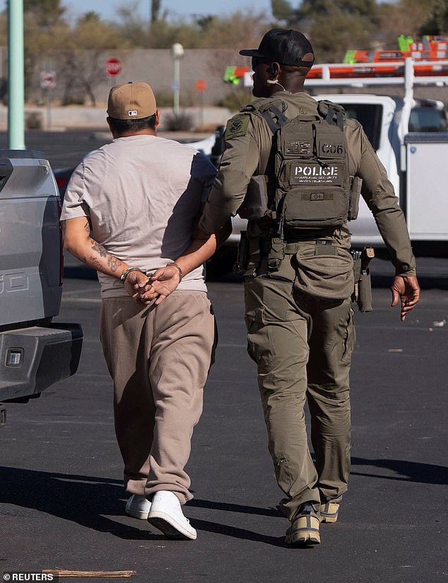 One of two documented immigrants with prior convictions detained by US Immigrations and Customs (ICE) Homeland Security Investigations (HSI) agents, walks handcuffed as an agent holds his arm, at a Home Depot parking lot in Tucson, Arizona on January 26, 2025