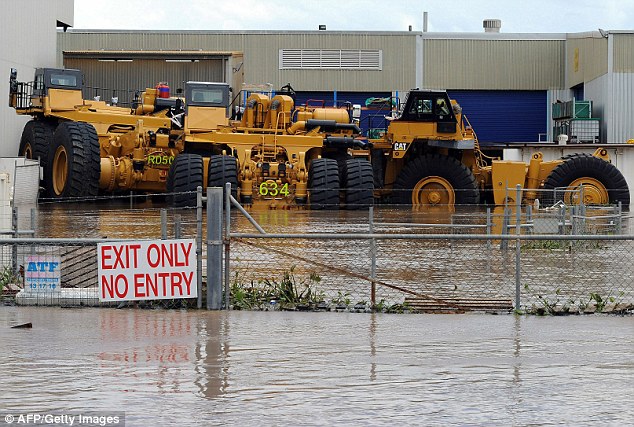 Crippled: Mining trucks are part-covered by water. Three quarters of coal mines in Queensland have been shut by the flooding