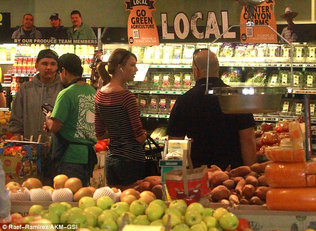 Security detail: The country-pop starlet - chatting with her bald bodyguard - listened to tunes on her iPhone as she attempted to blend in with shoppers