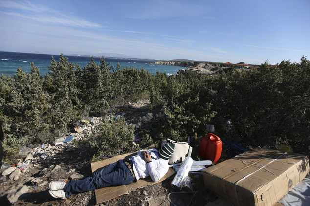 A migrant man sleeps as he waits for a chance to begin his effort on dinghy to try to cross from the Turkish coast to the Greek island of Chios, near Cesme, ...