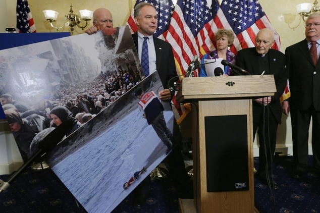 Senator Tim Kaine holds news photographs of Syrians during a news conference with national religious leaders to call on lawmakers to engage in policymaking a...