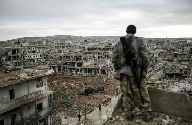 Musa, a 25-year-old Kurdish marksman, stands atop a building as he looks at the destroyed Syrian town of Kobane, also known as Ain al-Arab, on January 30, 2015