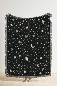 a black and white blanket with stars, planets and the moon on it in front of a person's feet