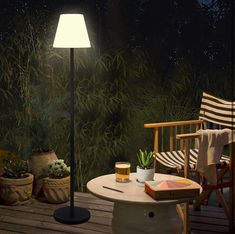 a lamp sitting on top of a wooden table next to a chair and potted plant