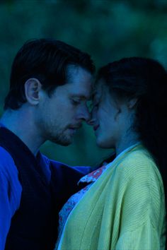 a man and woman standing next to each other in front of some trees at night