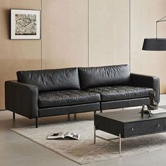 a black leather couch sitting in a living room next to a coffee table and lamp