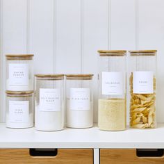 five jars with pasta in them sitting on a shelf next to other containers and drawers