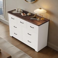 a white dresser with drawers and a mirror on the wall next to it in a living room