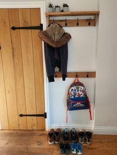 shoes are lined up in front of a coat rack with a backpack and hat hanging on it