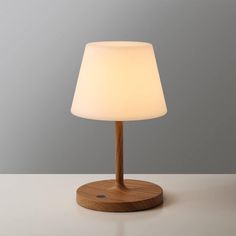 a wooden table lamp with a white light on it's base and a grey wall in the background