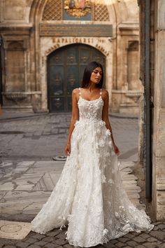 a woman in a white wedding dress standing on a brick walkway with an archway behind her