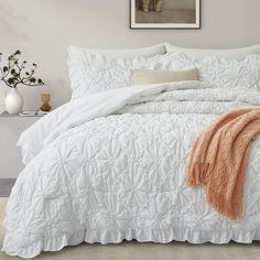 a bed with white comforter and orange throw blanket on top of it in a bedroom