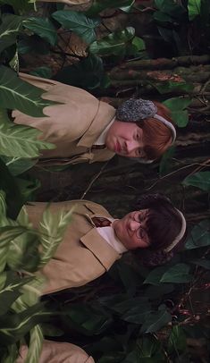 two women standing next to each other in front of green plants and leaves on the ground