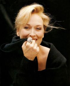 a woman with a ring on her finger smiles at the camera while wearing a black sweater