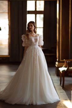 a woman in a white wedding dress standing on the floor with her hands behind her back