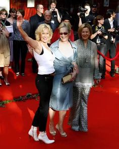 two women are standing on a red carpet with cameras around them and one woman is holding her arm up in the air