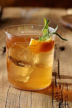 a glass filled with an orange and garnish on top of a wooden table